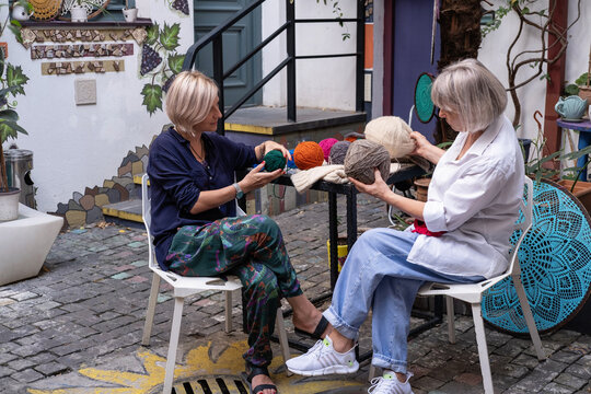 Elderly woman mother and adult daughter discussing knitting holding large balls of wool in their hands sitting in the garden in the yard