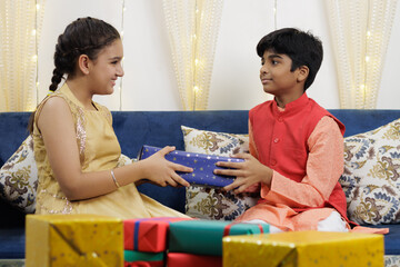 Kids, brother and sister friends siblings dressed up in ethnic wear exchanging gift box celebrating...