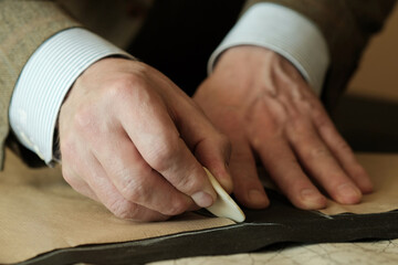 Obraz premium Sewing workshop. The hands of a tailor master. Close-up. Creating patterns of clothes on fabric with a tailor's pencil.