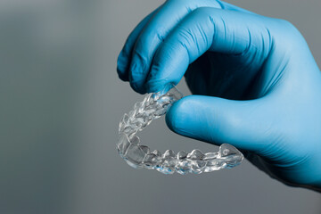 Dentist hand in blue gloves presenting a transparent removable aligner in front of dentistry room