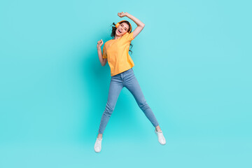 Full length photo of cute adorable girl dressed yellow t-shirt listening songs jumping high isolated teal color background