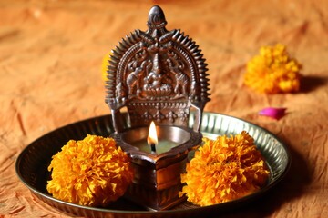 Lit oil brass Lakshmi/Gajalakshmi vilakku in a copper plate with marigold flowers/Diwali/Deepavali festival