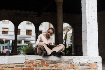 Stylish african american woman writing on notebook on urban street in Treviso.