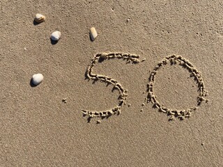 On the beach in the sand is carved the number 50
