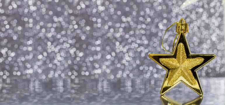 Gold bronze Christmas star on a defocused silver Christmas lights background with reflection. Decoration for the Christmas tree. Banner