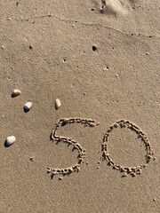 On the beach in the sand is carved the number 50