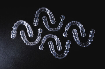 Close-up, invisible aligners on a black background in the form of a pattern. Plastic braces for teeth alignment