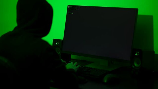 Hacker typing fast on a computer keyboard in a dimly lit room. Medium shot