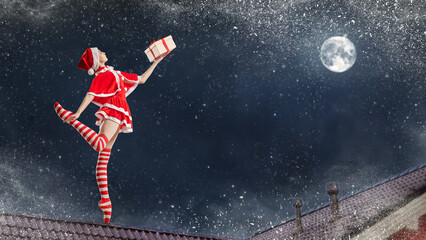 Dancing girl ballerina with a gift in her hands in a Santa Claus costume on the roof of a house on...