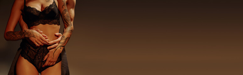 cropped view of young man hugging passionate tattooed woman in underwear isolated on brown, banner.