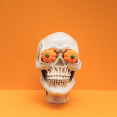 Realistic human skull with pumpkin eyes on orange color background. Funny spooky Halloween composition.