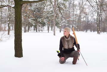 Young woman hunter hunting with bow and arrow in winter forest covered with snow