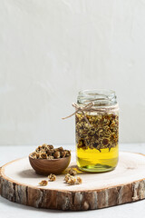 Jar of chamomile infused oil  with dried flowers on grey background with copyspace.