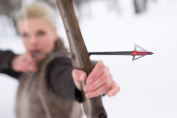 Young woman hunter hunting with bow and arrow in winter forest covered with snow