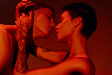 side view of passionate tattooed woman embracing and kissing young man isolated on red.