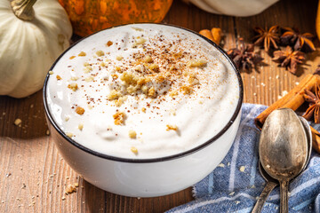 Bowl of homemade pumpkin spice yogurt ready for breakfast, with tart crumble topping. On wooden background with autumn pumpkins and spices, copy space