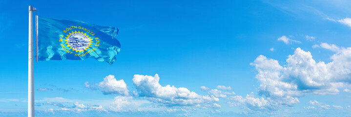 Fototapeta na wymiar South Dakota - state of USA, flag waving on a blue sky in beautiful clouds - Horizontal banner 