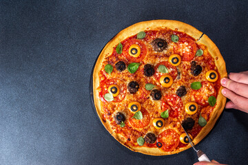 Halloween creative food. funny monster pizza decorated with creepy eyes, on black table background with Halloween party decoration top view copy space