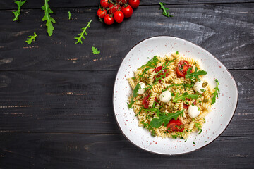 Caprese salad Pasta with tomato, mozzarella vegetable paste on a dark background, vegetarian salad, banner, menu recipe place for text, top view