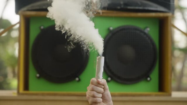 Hand moving smoke bomb or smoke grenade with big speaker on background, slow motion, sound syste