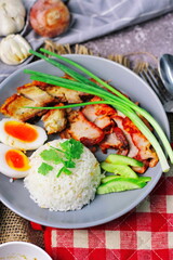 Thai dish '' Khao mu daeng '' or red sauce pork stew with rice and spring onions served in a gray plate on the black table in the restuarant
