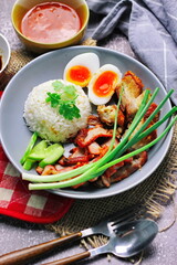 Thai dish '' Khao mu daeng '' or red sauce pork stew with rice and spring onions served in a gray plate on the black table in the restuarant