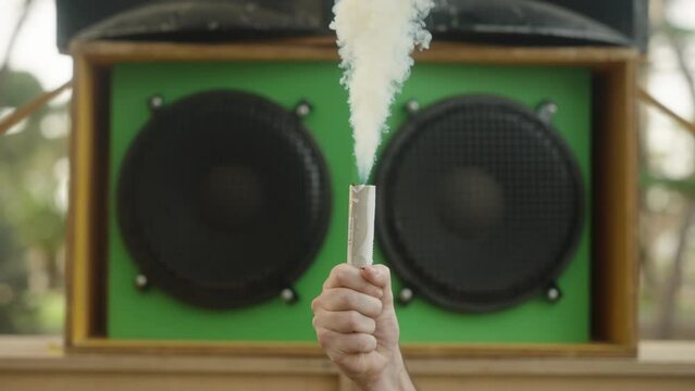Smoke bomb or smoke grenade in hand with big speaker on background, slow motion, sound system
