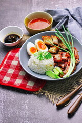 Thai dish '' Khao mu daeng '' or red sauce pork stew with rice and spring onions served in a gray plate on the black table in the restuarant
