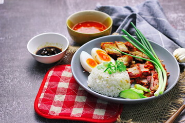 Thai dish '' Khao mu daeng '' or red sauce pork stew with rice and spring onions served in a gray plate on the black table in the restuarant