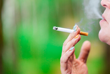 Middle age woman smoking cigarette at summer day,closeup.Blurred outdoors green background.Copy space.