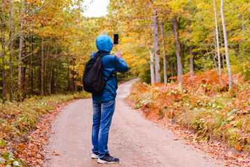 Man hiker stands in a beautiful autumn forest and catches a mobile network on a smartphone.Tourist looking for a cellular connection on a hike, raised his phone up.Travel Technology concept.
