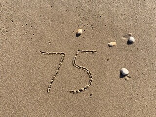 Fototapeta na wymiar On the beach in the sand is carved the number 75