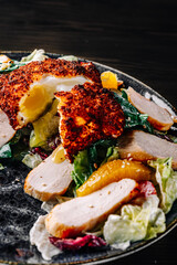 Salad with chicken, egg, tangerines and vegetables in plate on black wooden table background