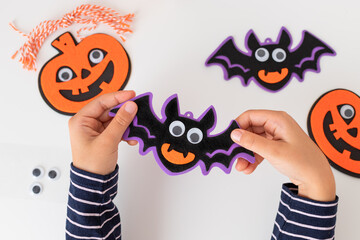 child hands holding halloween bat decorations with spooky face. Child craft holiday decor. closeup