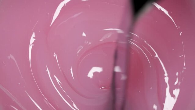 The spatula stirs the thick gel nail polish of pink color, close-up