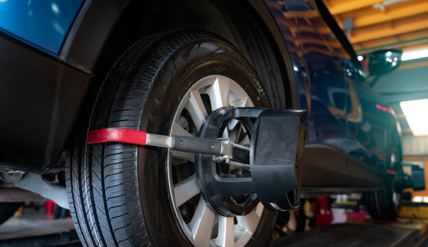 Wheel alignment equipment grip the tire of car wheel in car repair shop. Auto wheel alignment in workshop of service station. Car wheel balance. Suspension adjustment. Vehicle inside garage workshop. © Artinun