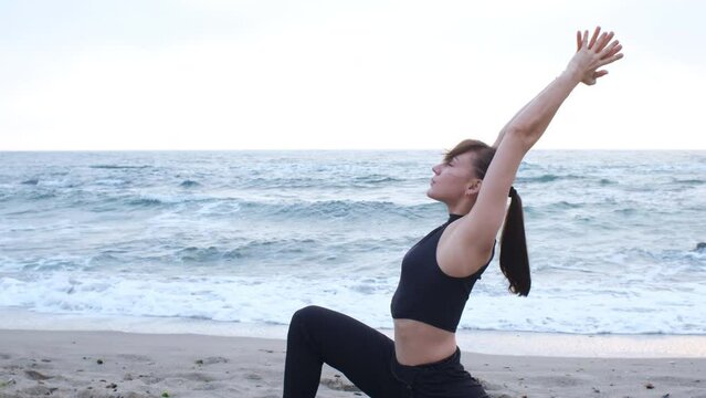 A caucasian young woman in a black sports suit doing yoga asana for woman's health care, on the ocean beach