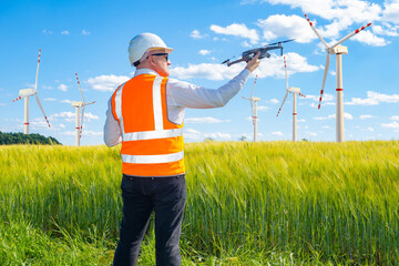 Wind farm engineer. Man with quadcopter and wind turbines. Man launches drone over wind farm. Work in field of regenerative energy. Guy explores windmills from air. Windmill owner in orange vest