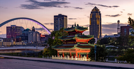 The Des Moines skyline, Women of Achievement Bridge, and Chinese Pavilion along the riverwalk at sunset.
