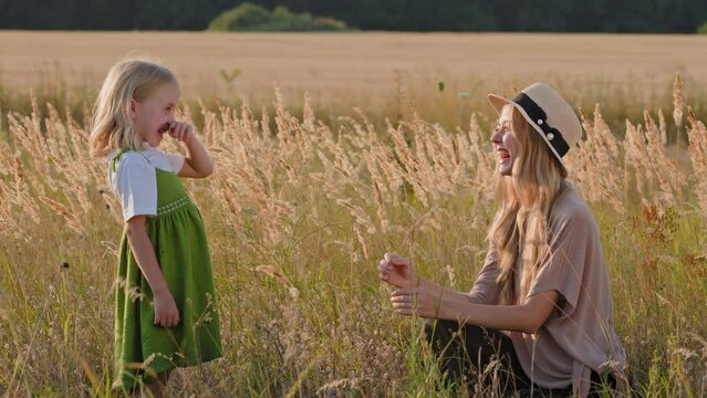 Caucasian mother with little daughter sitting in grass in golden field child sneezes allergies on dust fluff pollen allergy mother supports and talks woman in straw hat with small baby child outdoors