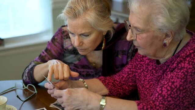 Closeup of elderly woman looks at photos with daughter. Senior woman sitting in the dining room looking at photographs with daughter. Brain training. Memory activity.