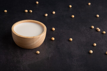 Soy milk in a wooden bowl with soytbeans on black bacground. Healthy eating lifestyle concept.