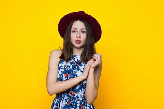 A young woman in a dress and hat on a yellow background.