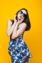 Brunette in a dress and sunglasses on a yellow background.