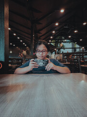 Young teen wearing glasses sitting at the table is using a  mobile phone.