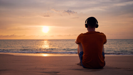 Rear view of man with headphones on beach. Serenity, contemplation and listening music at beautiful sunset.. - 536343547