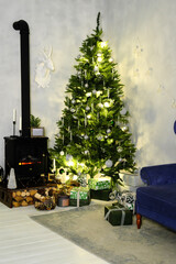 Evening Christmas atmosphere. The Christmas tree is illuminated by a garland, next to it is a sofa and an artificial fireplace