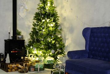Evening Christmas atmosphere. The Christmas tree is illuminated by a garland, next to it is a sofa and an artificial fireplace