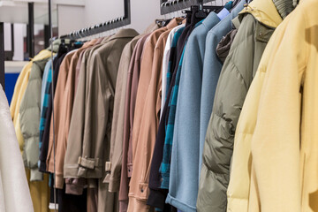 Warm coats in different colors and textures on hangers in the store. New autumn winter collection....