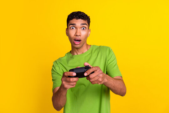 Photo of young handsome attractive student man hold wireless joystick playing excited crazy shock reaction player isolated on yellow color background